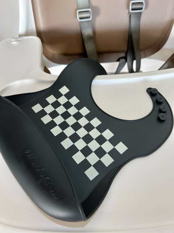 Black silicone food catcher bib with white checkered pattern on a high chair