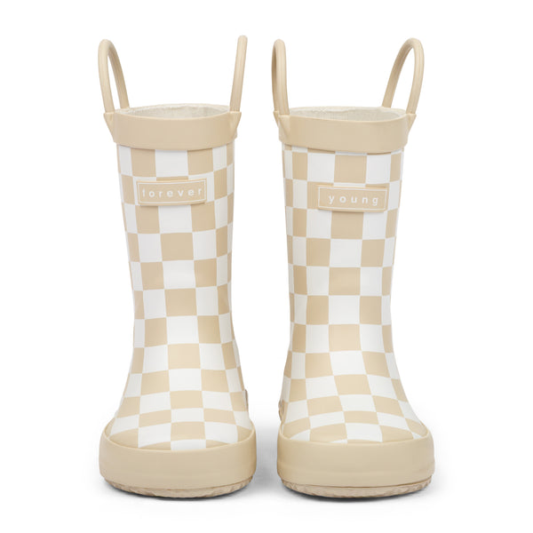 Front view of tan and white checkered children's rain boots with 'forever young' branding and grip handles for easy slip on, on a white background.
