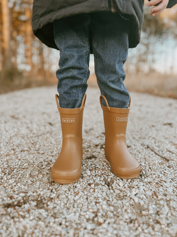 lifestyle images of child from waist down in jeans and a pair of Denver James rain boots in the solid color Golden standing on a gravel trail in the woods.