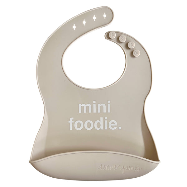 Front View of a light grey silicone food catcher bib with 'mini foodie.' text on a white background.