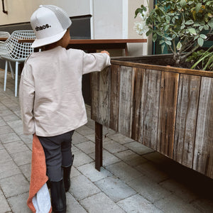 Child wearing a cap with 'chaos.' text, standing near a wooden planter outdoors.