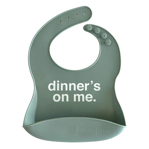 Front View of a seafoam silicone food catcher bib with 'dinner's on me' text on a white background.