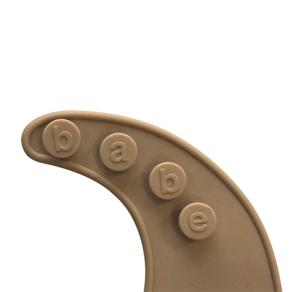 detail image of a beige Silicone bib on a white background with 'babe' buttons. 