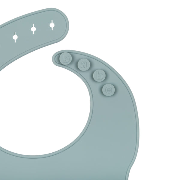 Back View of a blue/grey silicone food catcher bib on a white background with buttons that say 'babe'. 