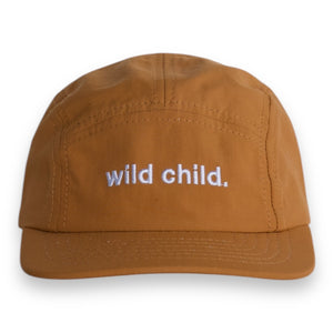 Front view of a brown five-panel cap with the words 'wild child.' embroidered on the front on a white backdrop. 