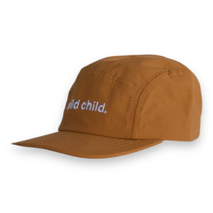 Front 3/4 view of a brown five-panel cap with the words 'wild child.' embroidered on the front on a white backdrop. 