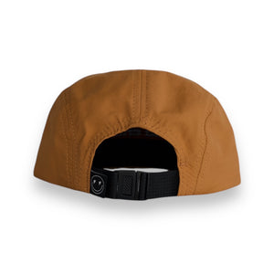 Back view of a brown five-panel cap with a tag that has a smily face with lighting bolt eyes on a white backdrop. The hat has a one snap closure. 