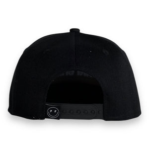 back view of black 5 panel black baseball cap with a snap back and smiley face with lighting bolt eyes tag on white backdrop. 