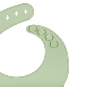 Detail View of a light green silicone food catcher bib on a white background with buttons that say 'babe'. 