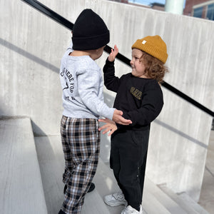 2 boys wearing sweatshirts and beanies standing on stairs high five ing. 