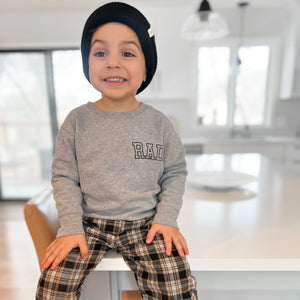 Boy sitting on table wearing sweatshirt that says 'rad'. 