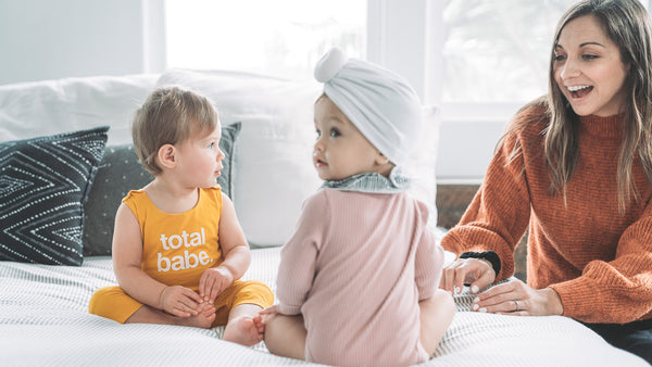 Mom watching two babies sit on Bed in rompers