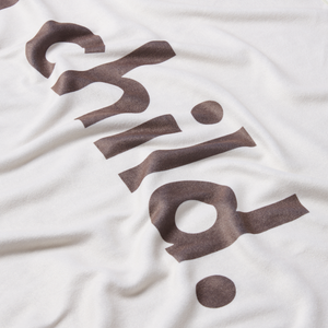 a detailed shot of a white or stone colored microfiber beach towel with the word 'child.' printed in large brown letters. 