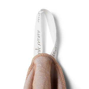 a detailed image of a hanging tag on a beige microfiber beach towel with 'denver james' printed in black cursive font on a white tag. 