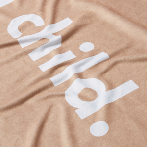 a detailed shot of a beige microfiber beach towel with the word 'child.' printed in large white letters. 