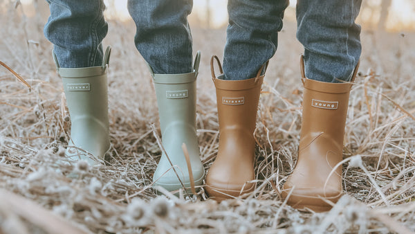 Two boys wearing toddler rain boots in a field. 