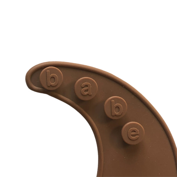 detail image of a dark brown silicone bib on a white background with 'babe' buttons. 