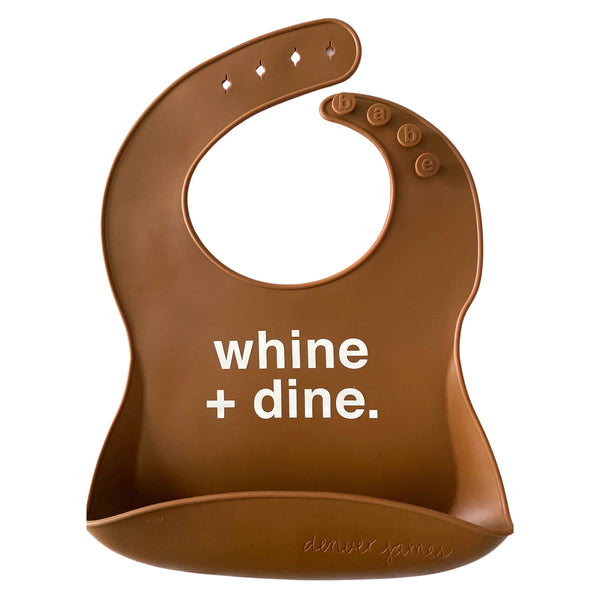 Front View of a dark brown silicone food catcher bib with white 'whine + dine.' text on a white background.