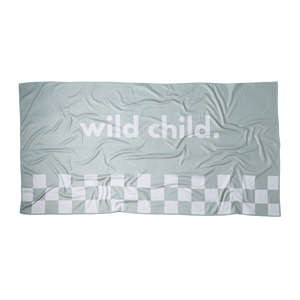 an overhead image of a green microfiber beach towel with racing checkers along the bottom and the words 'wild child.' printed in large white letters across the middle on a flat surface showing the rectangular dimension of the towel. 