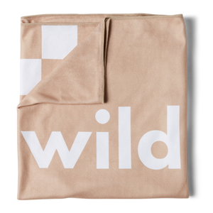 an overhead image of a beige beach towel folded into a square with the top left corner turned down revealing the checkered racing pattern in white with the word 'wild' printed in large white letters on the front. 
