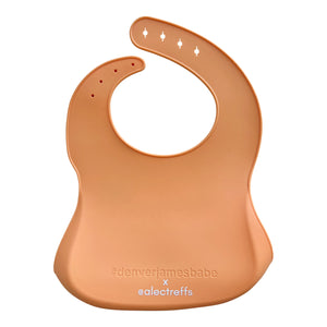 Back view of a coral silicone bib on a white background with '#denverjamesbabe' text and 'x @alectreffs' in white text. 