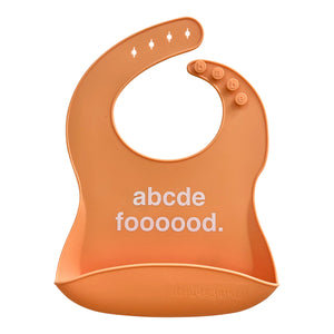 Front View of a coral silicone food catcher bib with white 'abcde foooood.' text on a white background.