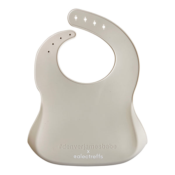 Back view of a light grey silicone bib on a white background with '#denverjamesbabe' text and 'x @alectreffs' in white text. 