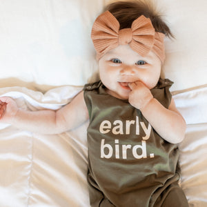 baby laying on bed in a romper that says 'early bird.'