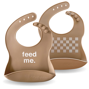 Two brown baby bibs with one saying 'feed me.' on a white background