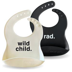 Two baby bibs, one beige with 'wild child.' and one black with 'rad.', on a white background.